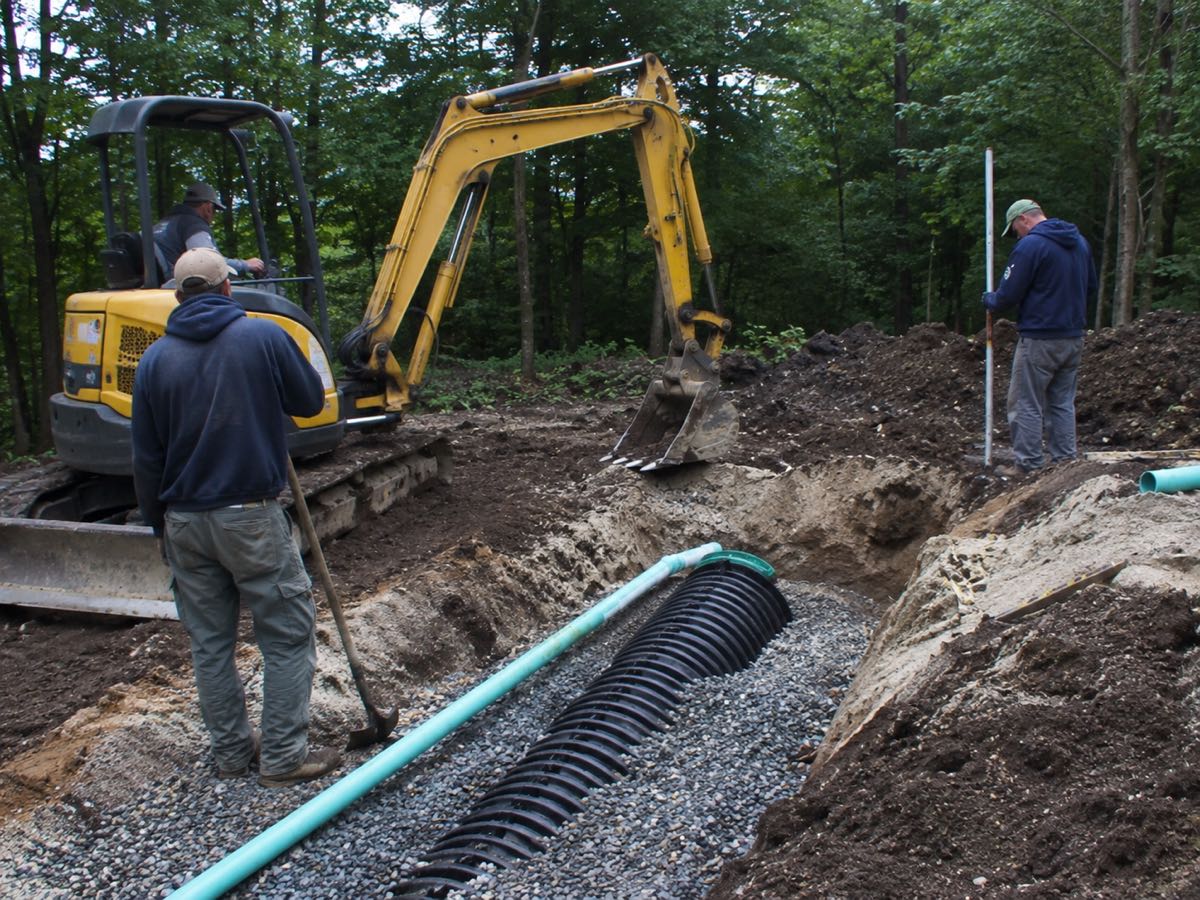 Mini excavator installing drain field chambers in a wooded lot